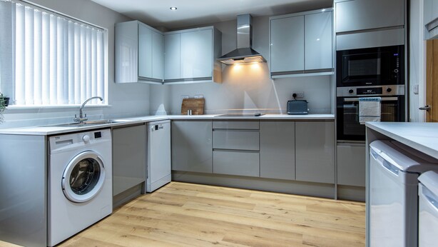 A modern kitchen with grey cabinets, a built-in washing machine, and a microwave. - Langdown House (Nottingham)