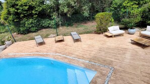 Un espace aménagé au bord de la piscine, avec une terrasse en bois, une piscine et du mobilier d’extérieur comprenant un canapé et des fauteuils.