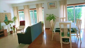 A spacious living area with a sofa, dining table, and chairs, large windows with curtains, and potted plants. - Welcome to SINTRA HOME, a haven between green hills and the blue Atlantic. (São João das Lampas)