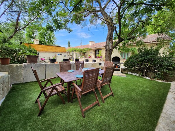 Un patio con mesa y sillas, rodeado por un césped cuidado y un muro de piedra.