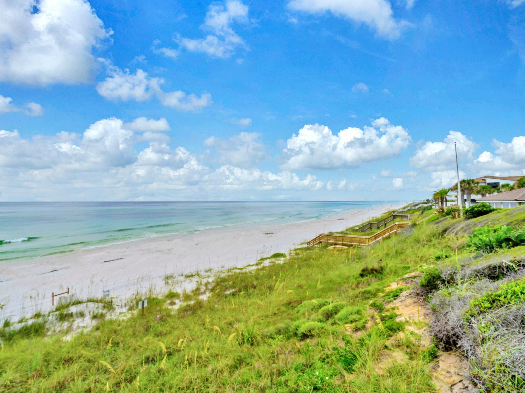 A beach with a wooden boardwalk, grassy areas, and a clear sky.