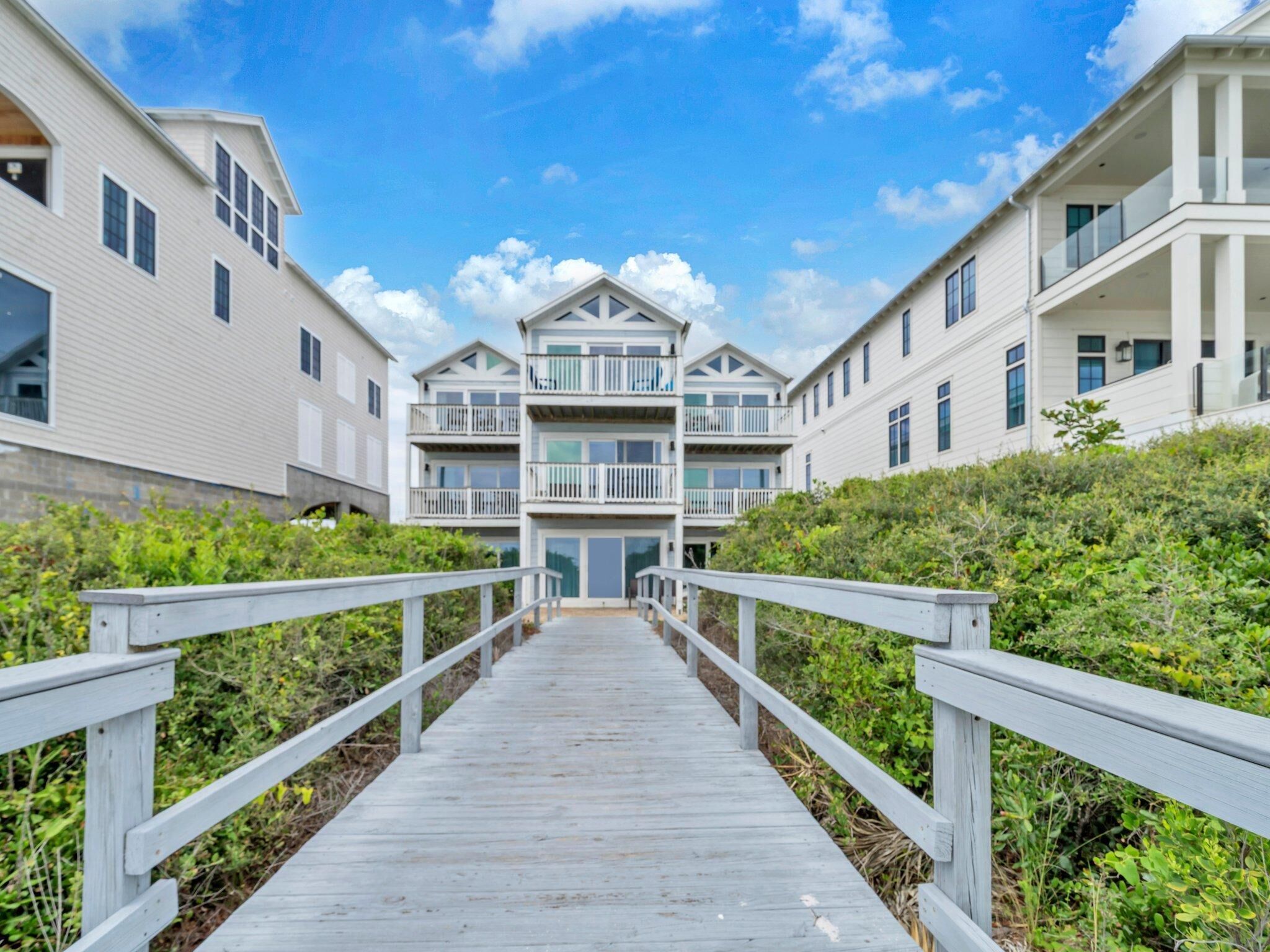 A wooden boardwalk leading to a multi-story building with balconies, surrounded by greenery.