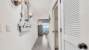 Un pasillo con una cocina moderna a la vista, visible a través de una puerta abierta, que incluye un refrigerador y una mesa de comedor con sillas.