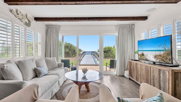 Un salón espacioso con un televisor grande, asientos cómodos y vistas a la playa a través de amplias ventanas.