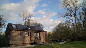 Eine kleine, rustikale Holzhütte mit geneigtem Dach, Solaranlagen und einem Schornstein.