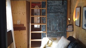 Ein gemütliches Dachzimmer mit Schlafplatz in der Mansarde, Holzwänden, Kamin und einer kleinen Bücherregal.