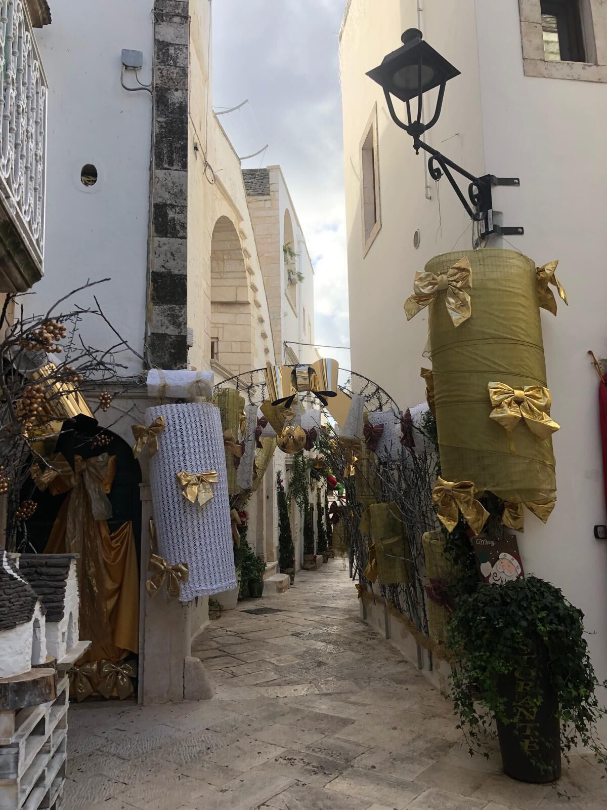 Una calle estrecha flanqueada por edificios adornados con lazos y guirnaldas doradas, lo que sugiere un evento festivo o cultural.
