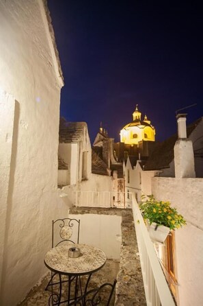 A narrow alleyway with a table and chair, leading to a brightly lit building with a dome. - Bella Itria (Locorotondo)