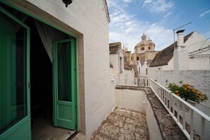 A narrow alleyway with a green door leading to a room, a white railing with flowers, and a building with a dome in the background. - Bella Itria (Locorotondo)