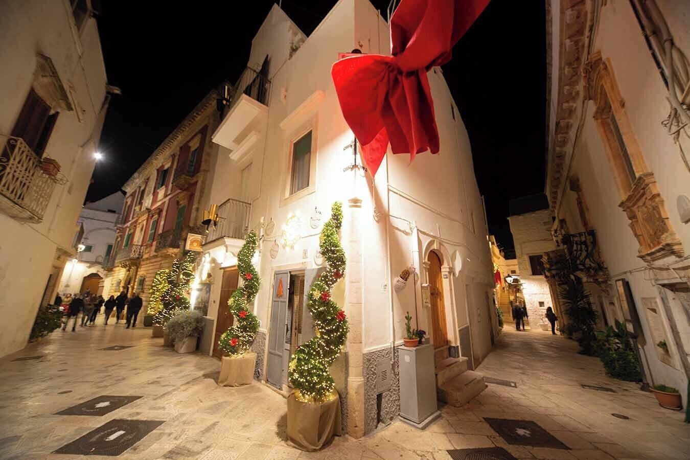 A narrow street with buildings on either side, decorated with Christmas trees and lights.