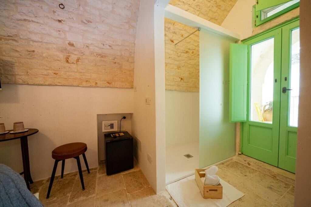 Une pièce avec un mur en pierre, une porte verte, une petite table avec un tabouret et une prise de courant.