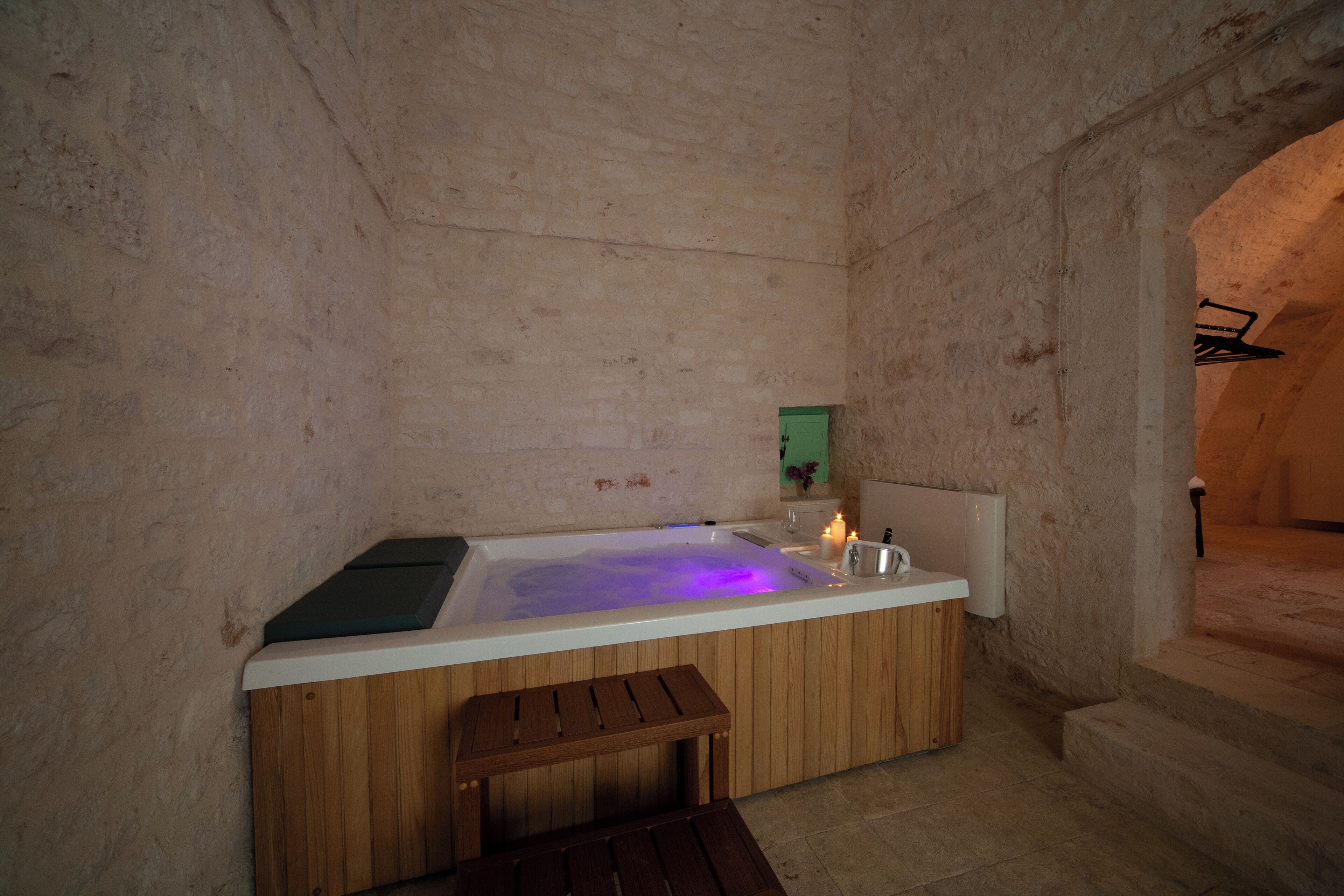 A stone-walled room with a wooden bench, a bathtub with a green towel, and a small table.