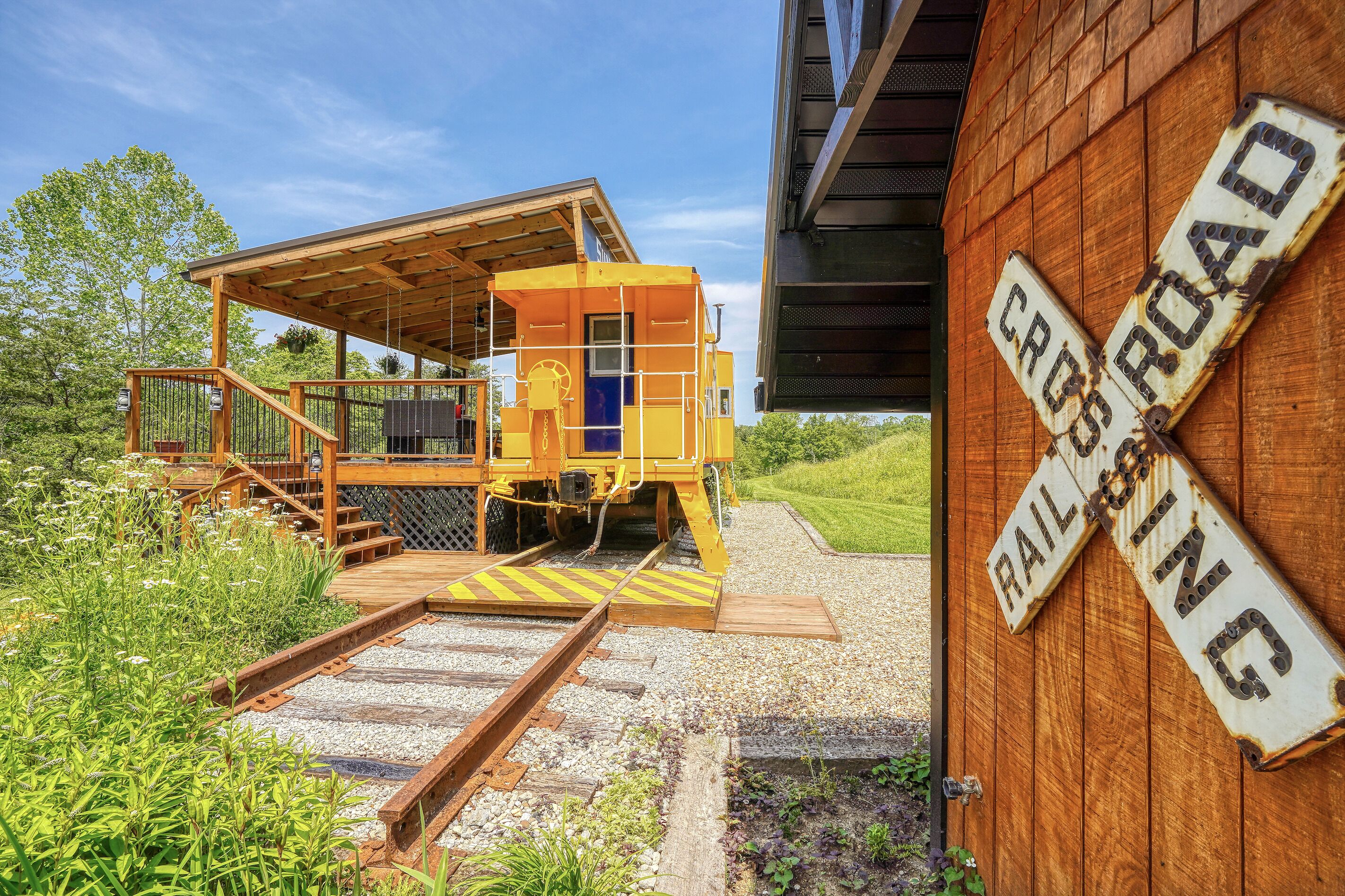 Una estructura amarilla de señal ferroviaria con una plataforma de madera y escaleras, rodeada de vegetación y grava.