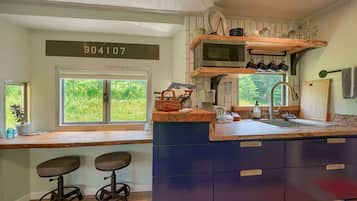 A kitchen with a wooden countertop, two stools, a microwave, and a sink.