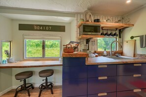 A kitchen with a wooden countertop, two stools, a microwave, and a sink.