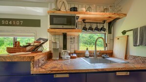 Une cuisine moderne dotée d’un plan de travail en granit, d’un four à micro-ondes, de tasses suspendues et offrant une vue sur la verdure à l’extérieur.