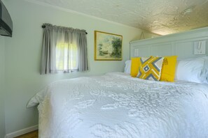 Ein Schlafzimmer mit einem großen Bett, einem Fenster mit Vorhängen, einem Gemälde an der Wand und einer Decke mit strukturierter Gestaltung.