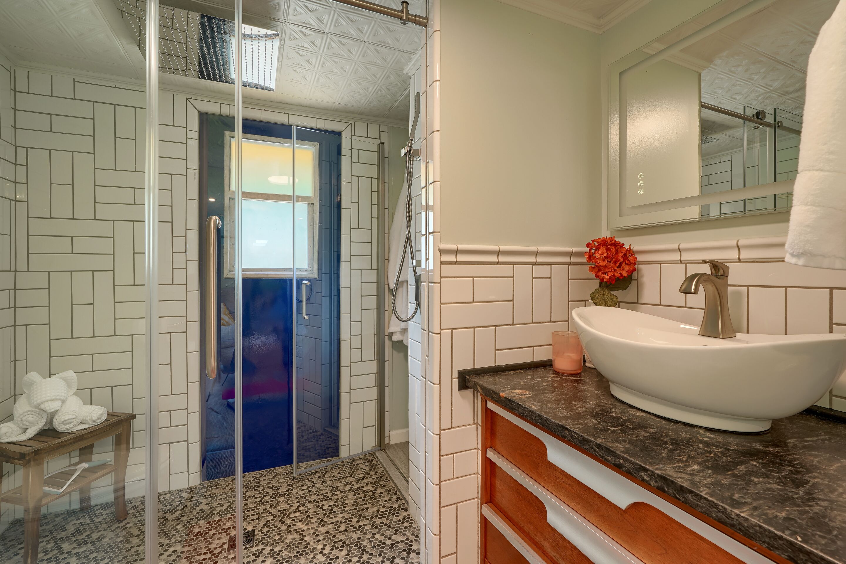 A modern bathroom with a glass shower enclosure, a white sink with a marble countertop, and a mirror above the sink.
