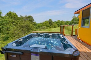 Ein Whirlpool auf einer Holzdiele mit Blick auf ein Wiesfeld und Bäume.