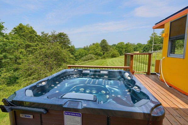 Un jacuzzi en una terraza de madera, con vista a un campo cubierto de césped y árboles.
