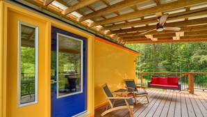 Une terrasse en bois avec une porte bleue, un canapé rouge et deux fauteuils à bascule.