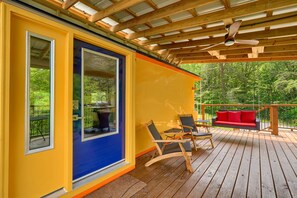 A wooden deck with a blue door, a red sofa, and two rocking chairs.