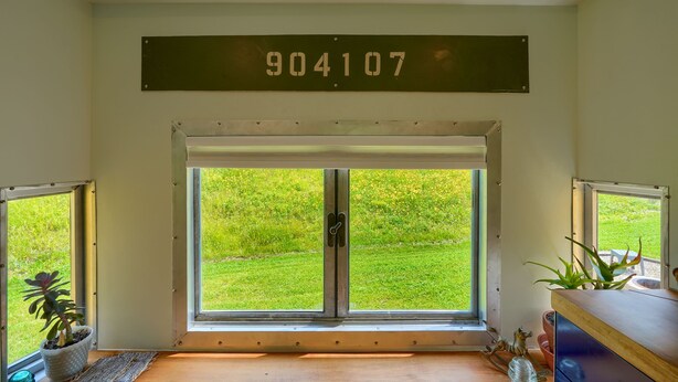 Une pièce dotée d’une grande porte-fenêtre coulissante donnant sur un espace extérieur verdoyant, d’une plaque métallique portant le numéro 904107 et d’une petite plante en pot posée sur le rebord de la fenêtre.