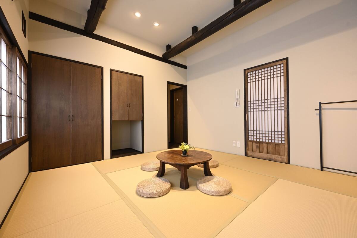 Ein Raum mit Tatami-Matten, einem runden Tisch, Holztüren, die sich verschieben, und einem Shoji-Bildschirm.