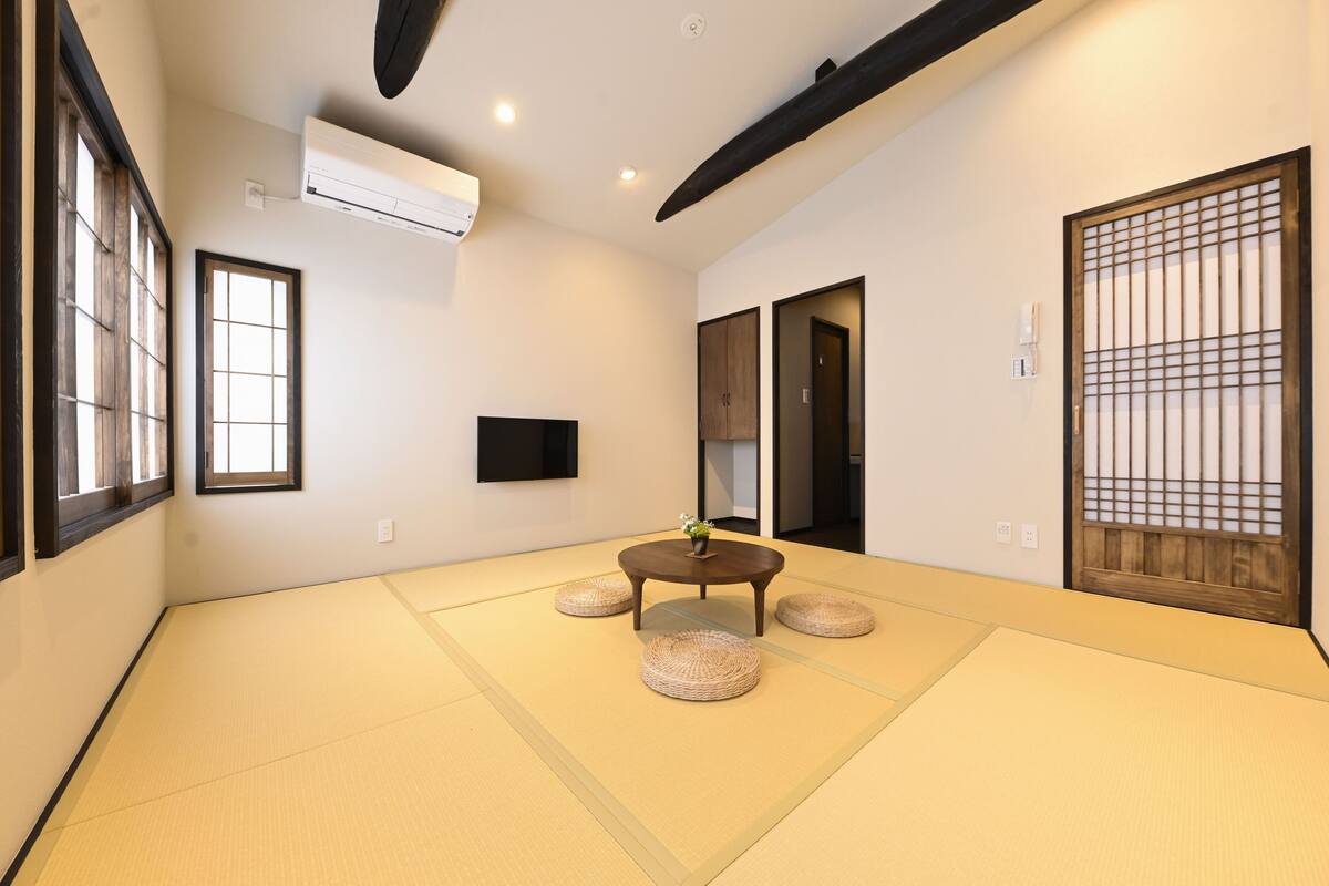 Ein Raum mit Tatami-Matten, einem Tatami-Tisch, einer Wand-Klimaanlage und einer Schiebetür mit Holzgittermuster.