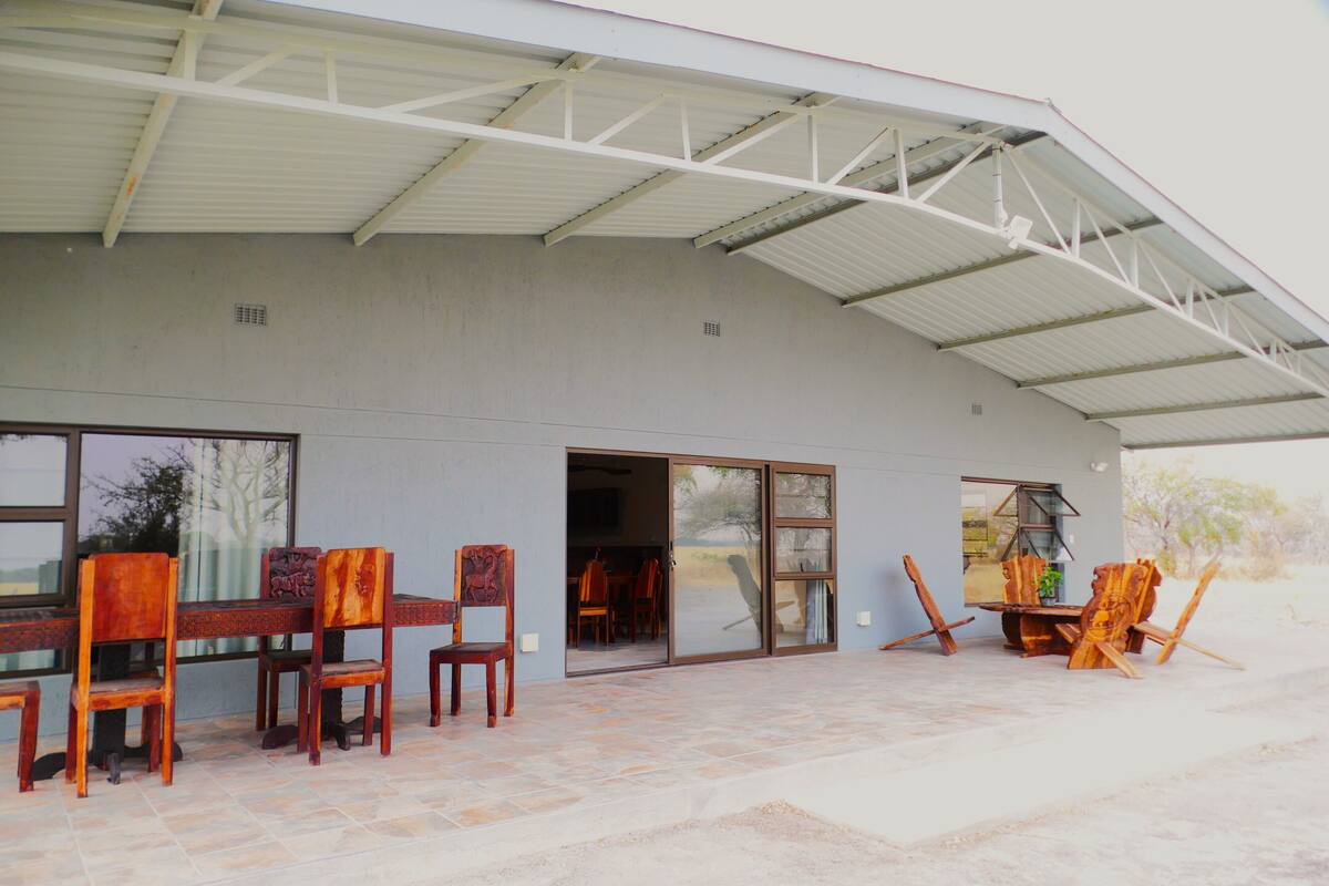 An outdoor patio with a covered seating area, a dining table with chairs, and a painting easel.