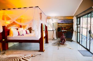 A spacious bedroom with a large bed, a canopy, and a view of the outdoors through large windows.