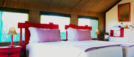 A room with two beds, each with red headboards, white bedding, and purple pillows. There are two bedside tables with lamps, a mirror, and a small shelf with items.