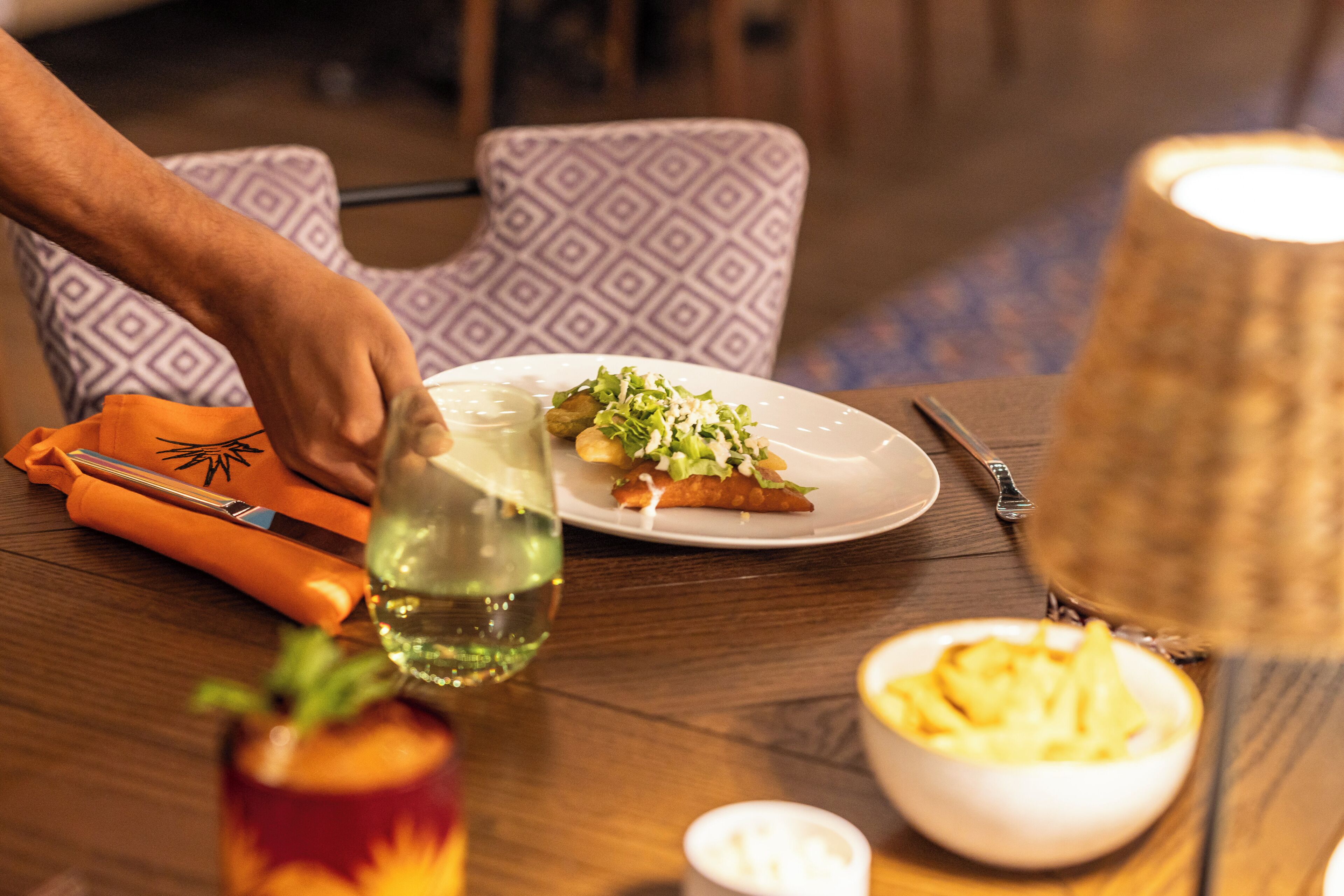 A dining table with a plate of food, a glass of water, and a bowl of chips.