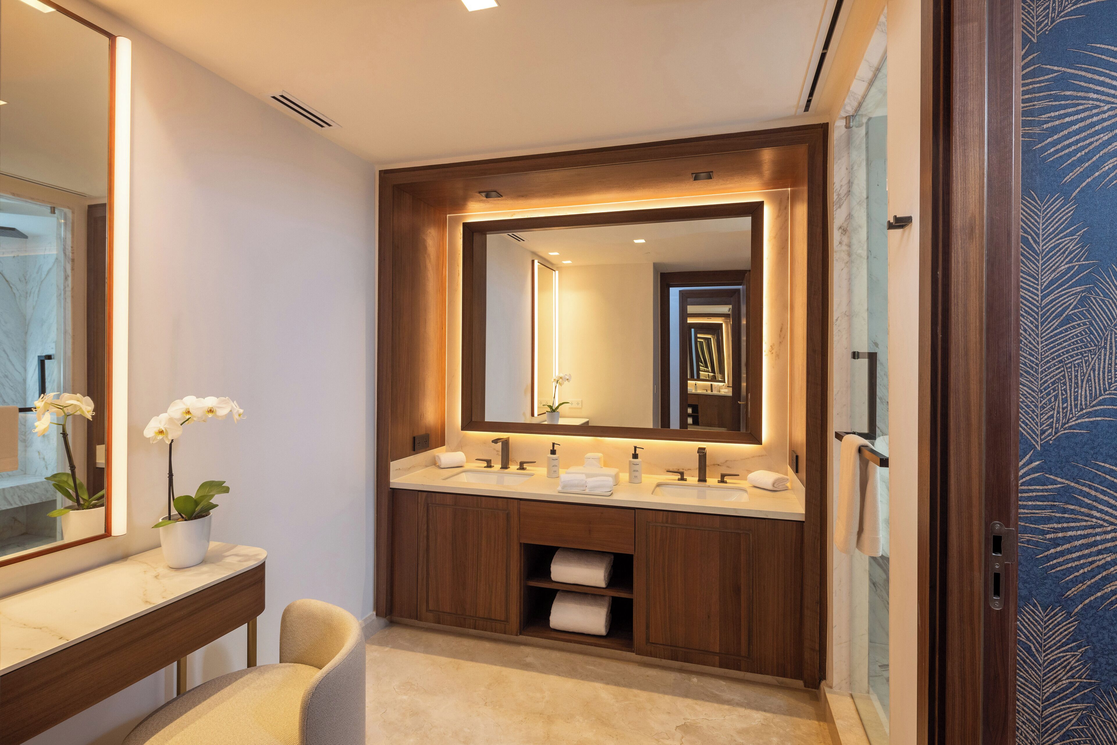 A modern bathroom with a large mirror, two sinks, a vanity, and a potted orchid.