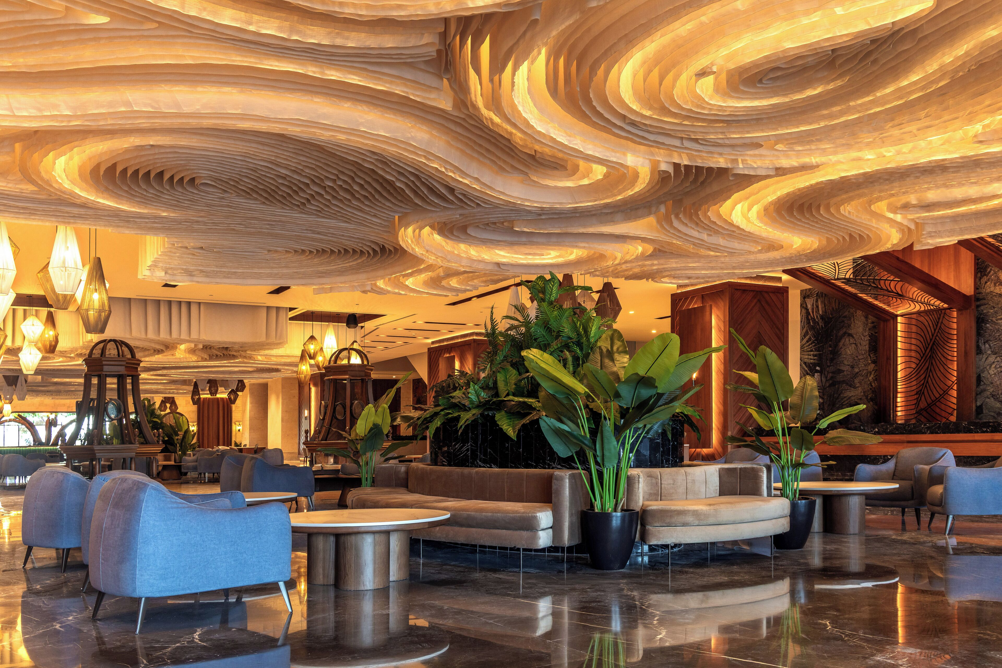 Un hall d’entrée doté d’un plafond au design moderne, d’espaces aménagés pour s’asseoir et de plantes en pot.