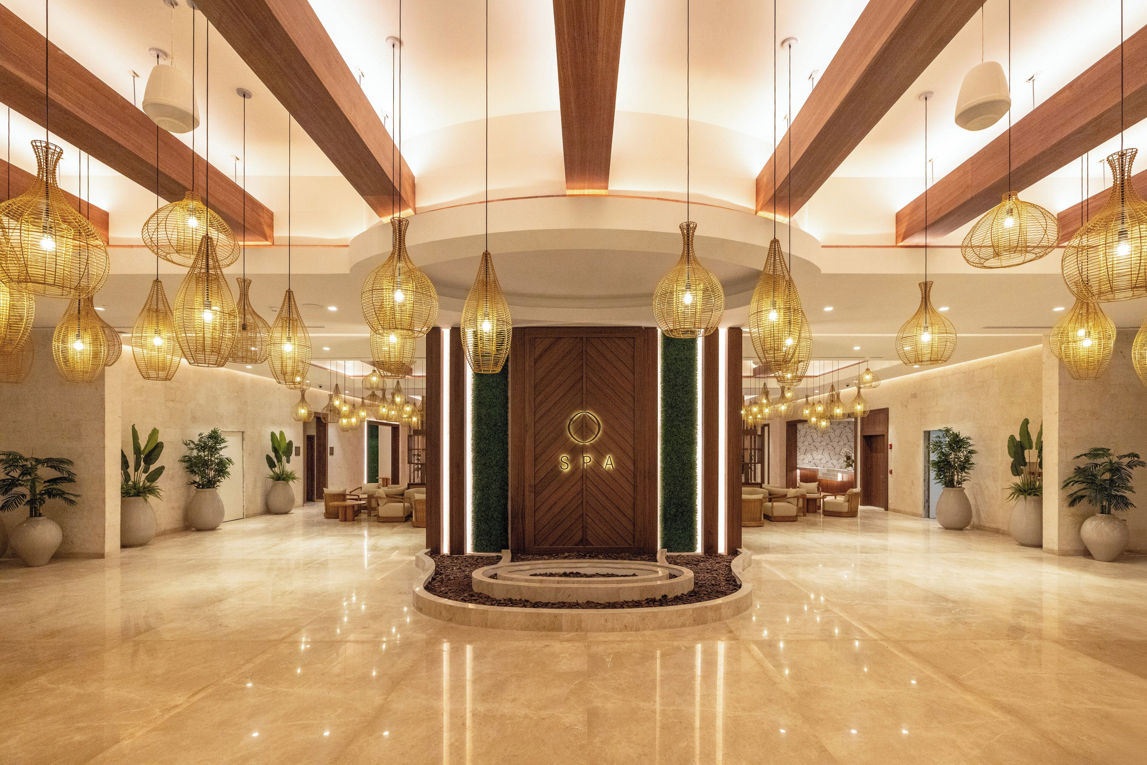 A spacious lobby with a central reception desk, multiple hanging light fixtures, and potted plants.