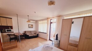 A bedroom with a bed, a wardrobe, a desk, a chair, a sofa, and a window with curtains.