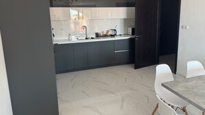 A modern kitchen with dark cabinets, a white countertop, and a dining area with white chairs and a marble table.