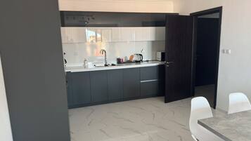 A modern kitchen with dark cabinets, a white countertop, and a dining area with white chairs and a marble table.