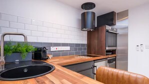 A modern kitchen with a wooden countertop, a sink, a coffee machine, and a built-in oven. - Studio37 - A cosy, stylish central hideaway | Pass the Keys (Cirencester)