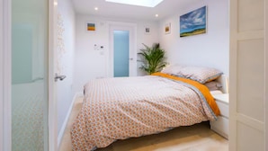 A bedroom with a skylight, a bed with patterned bedding, a bedside plant, and a painting on the wall. - Studio37 - A cosy, stylish central hideaway | Pass the Keys (Cirencester)