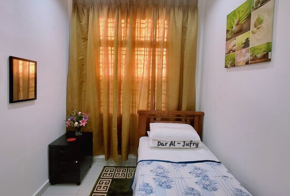 A bedroom with a bed, a nightstand with a vase of flowers, a wall-mounted picture, and a curtain. - HOMESTAY DAR AL - JUFRY (Kuantan)