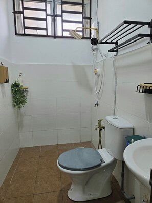 A small bathroom with a toilet, bidet, and sink. There is a window with a black frame and a showerhead mounted on the wall. - HOMESTAY DAR AL - JUFRY (Kuantan)