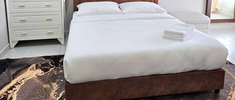 A neatly made bed with white linens, a brown headboard, and a decorative flower arrangement on a bedside table.