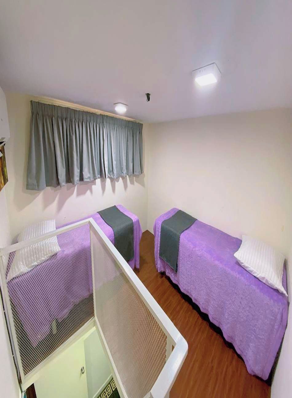 A small, simple room with two beds, a window with a curtain, and a white bed frame.