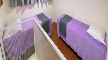 A small, simple room with two beds, a window with a curtain, and a white bed frame.