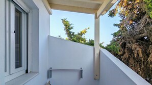 Un petit balcon avec une table et des bancs en bois, une fenêtre et une vue sur des arbres et un immeuble.