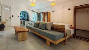 Une chambre à coucher moderne avec un lit en bois, un banc et, au fond, un coin cuisine.