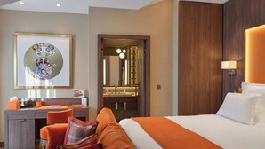 Ein Hotelzimmer mit einem Bett, einem Schreibtisch, einem Sessel, einer Couch, einem großen Spiegel und einer Wandlampe.