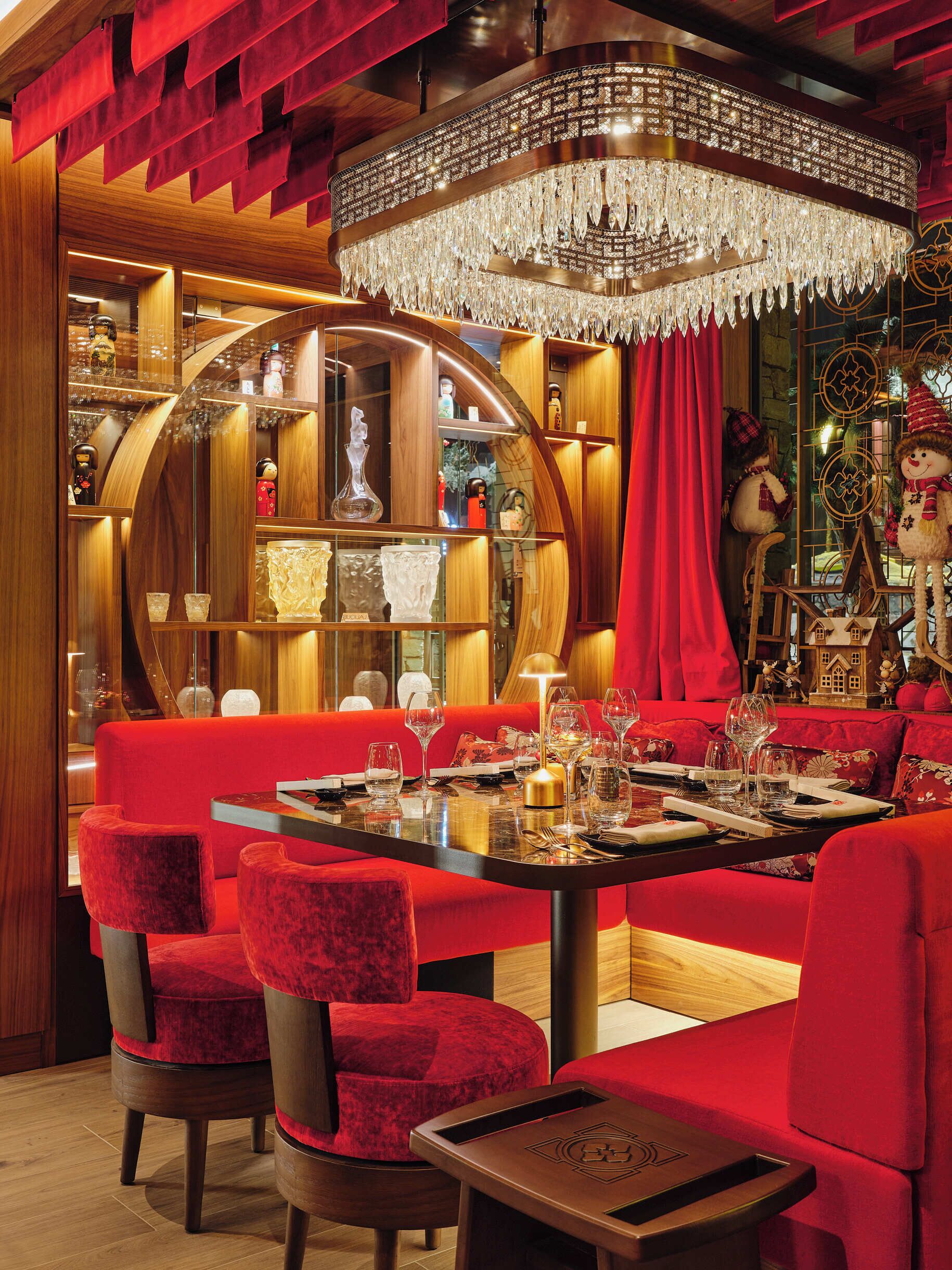 A dining area with a chandelier, red upholstered seating, and wooden accents.